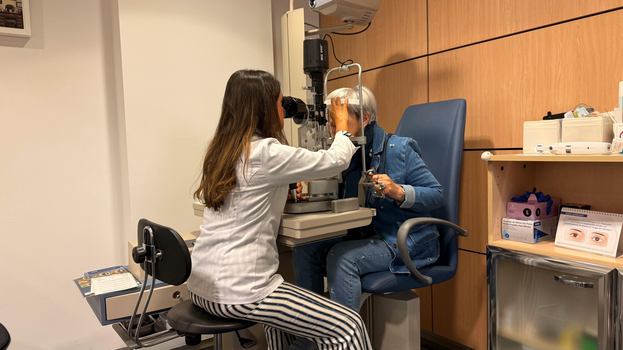 Optometrist performing an eye exam with a slit lamp in a well-lit examination room.